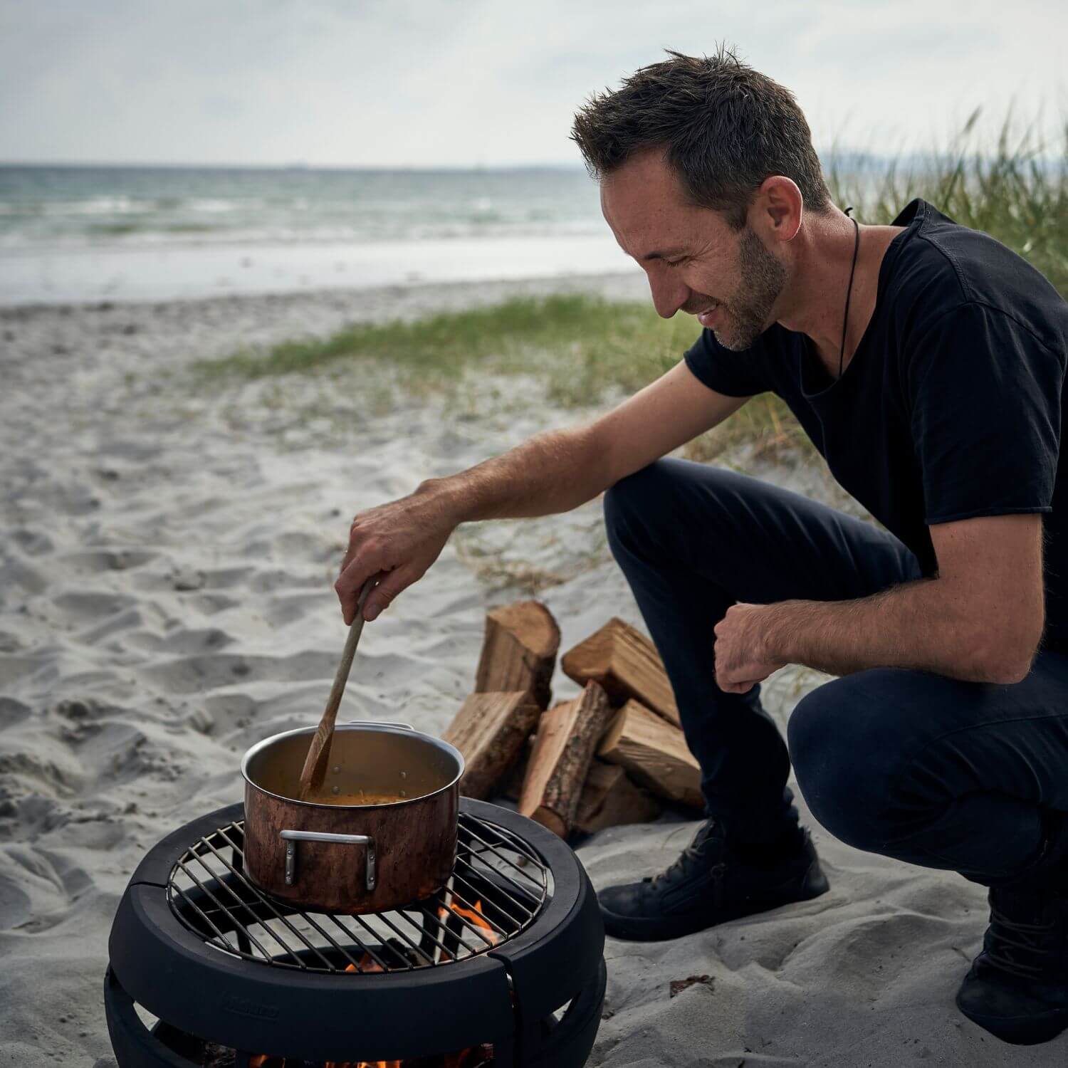 Mand laver mad over bålfad på stranden