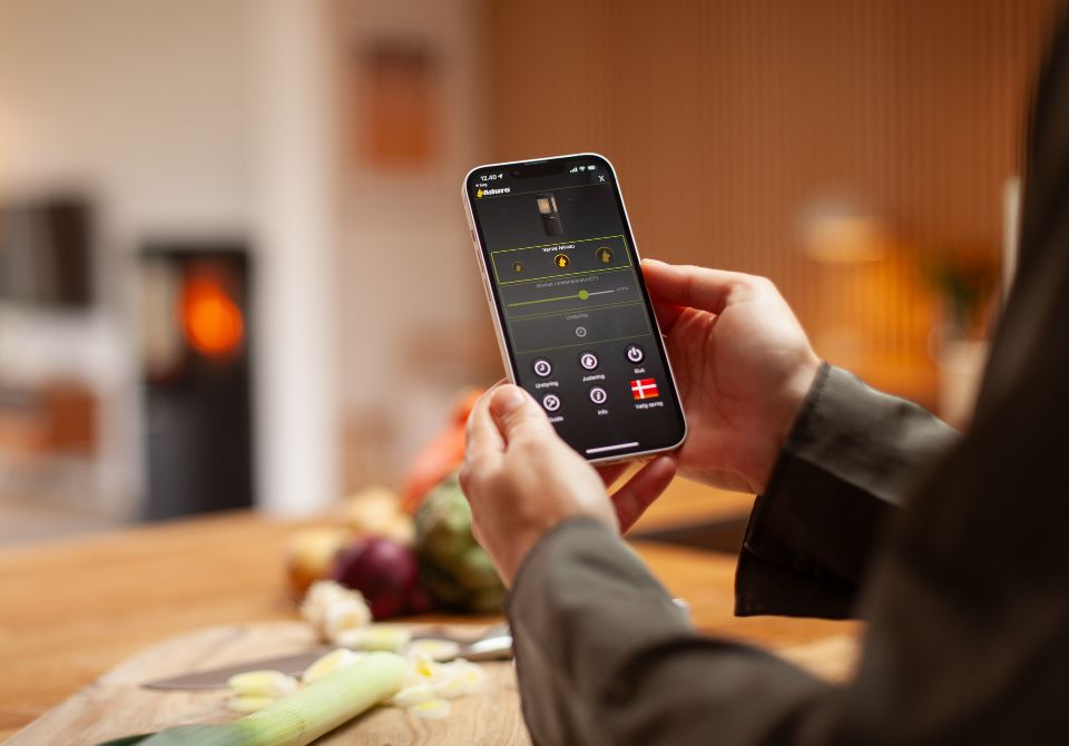 To hænder holder smartphone med Hybrid App foran brændende hybridovn